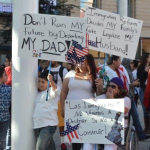 一个家庭在集会上举着牌子。 标语上写着：“孩子正遭受遣返的迫害”，“不要通过驱逐我的父亲而毁了我的未来！”，“移民改革决定了我家庭的命运。现在使我的丈夫合法化！”和“'失去移民'的没有维尼莫斯A DestruirSíNo Construir！”