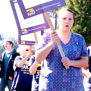 A line of SEIU members marching on a picket line. The sign in the foreground reads "No forced overtime"
