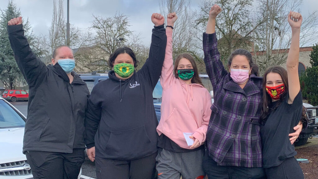 Five young women wearing cloth face masks standing together with raised fists