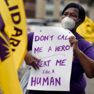Trabajador con un cartel que dice "No me llames héroe / Trátame como a un HUMANO"