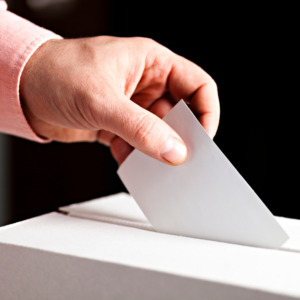 рука кладет бюллетень в урну для голосования