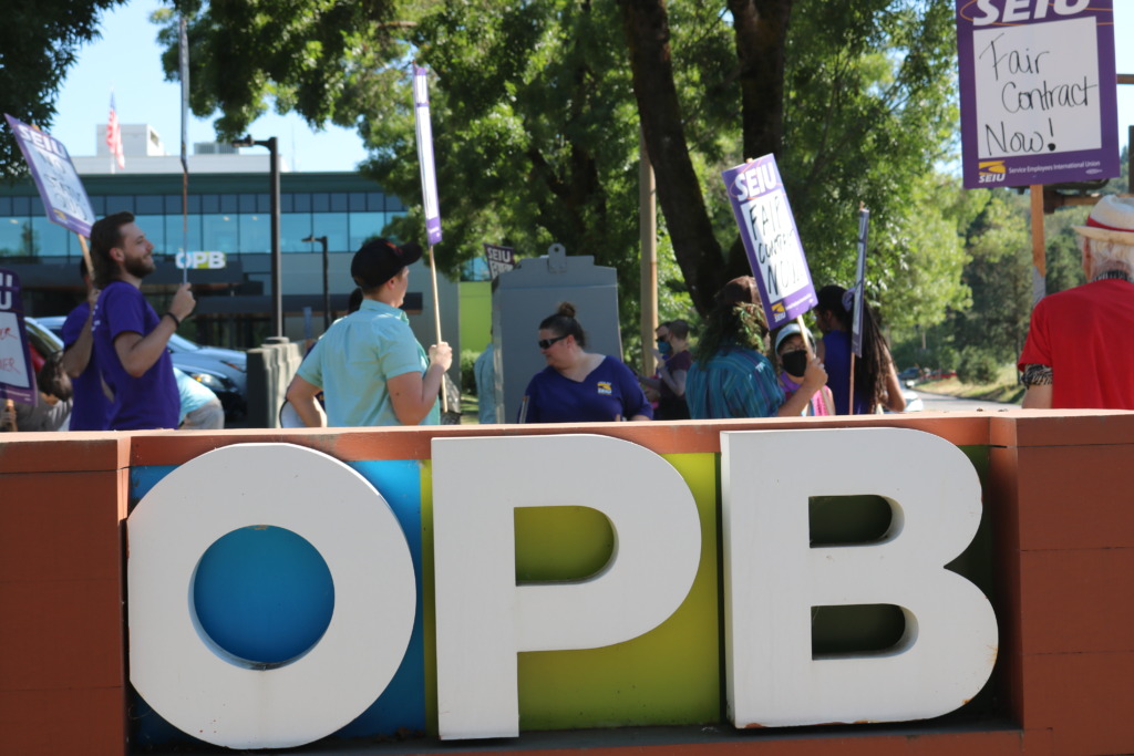 Union members wearing purple and holding signs saying "Fair Contract Now" behind a large OPB sign. They are at the OPB Headquarters.
