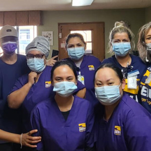 Группа работников дома престарелых SEIU в масках и фиолетовых халатах.