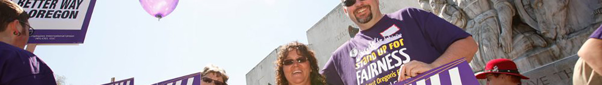 Một nhóm thành viên SEIU mỉm cười đeo kính râm và áo phông màu tím, cầm biển hiệu SEIU bên ngoài trước tòa nhà Tòa nhà Đại hội Bang Oregon. Một quả bóng màu tím hiển thị ở nền