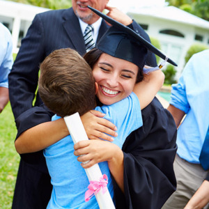 Una mujer sonriente con toga y birrete y sosteniendo un diploma, abrazando a un niño
